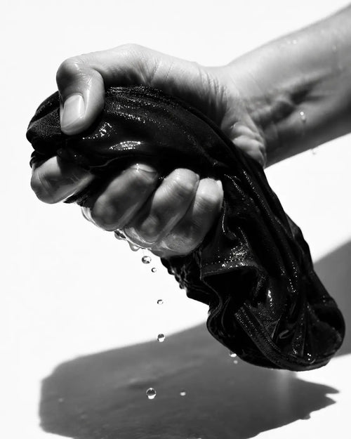 a hand squeezing water out of a black underwear