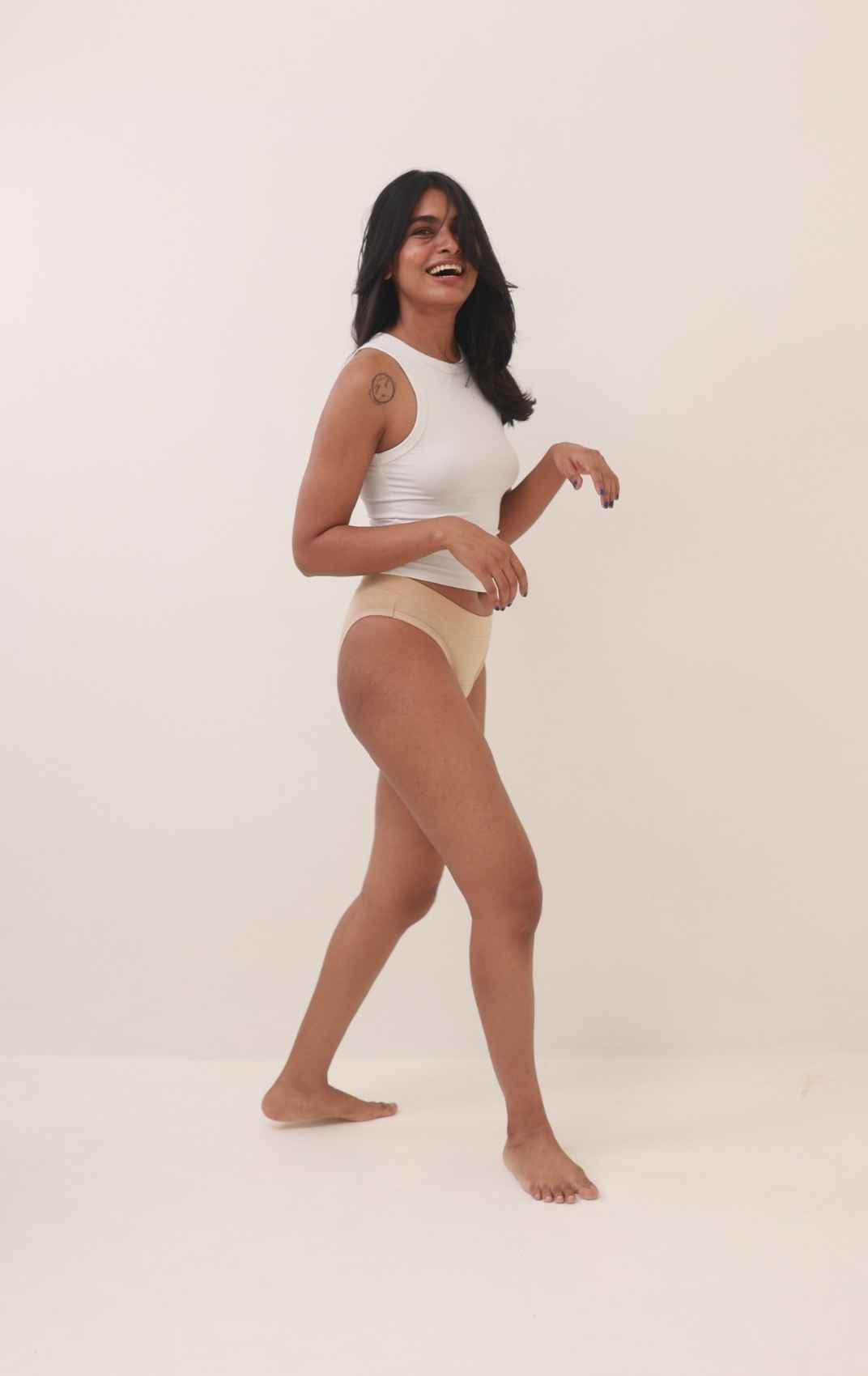 Ride or Dry leakproof underwear in Oatmeal: a woman in a white sleeveless top and beige high-waisted briefs against a plain off-white studio background.
