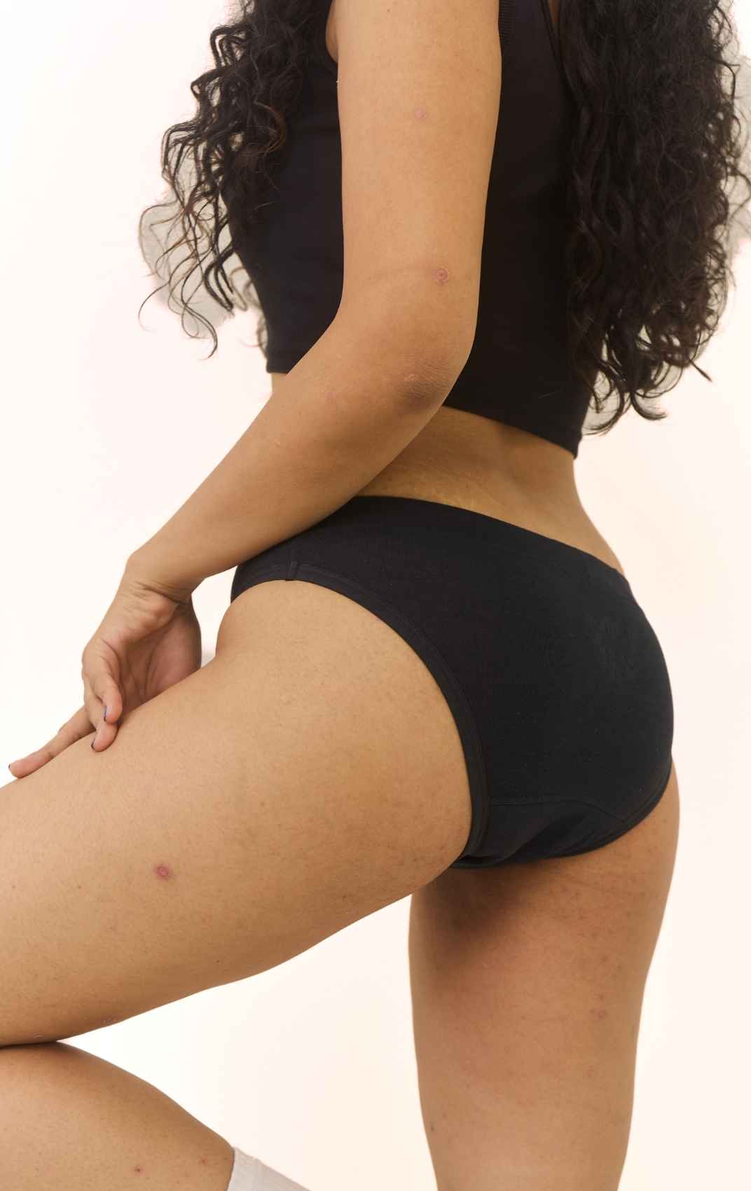 Ride or Dry leakproof underwear in Volcanic Black: side-rear view of a woman in black underwear and a black crop top against a plain light background.